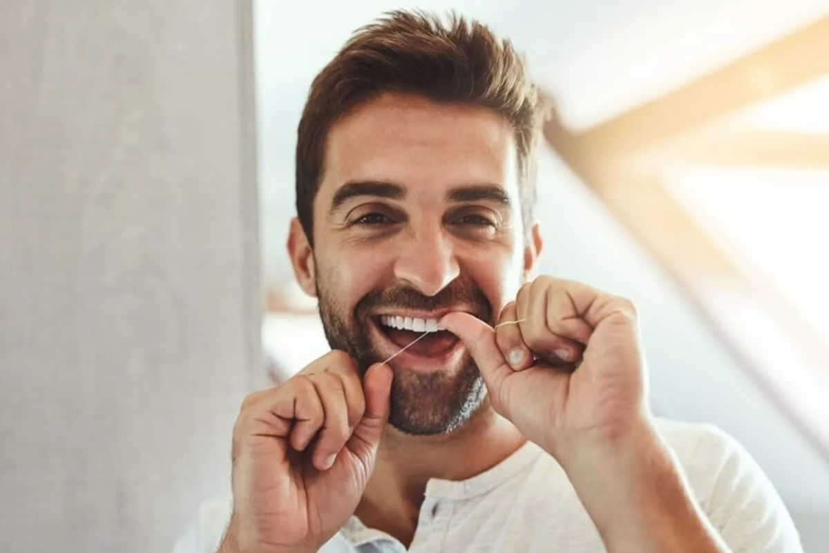 A patient flossing and smiling in a bright bathroom